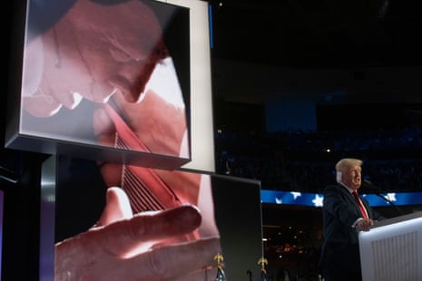a man with a bandage on his ear talks to an audience in front of an image of himself taking cover from a gunman