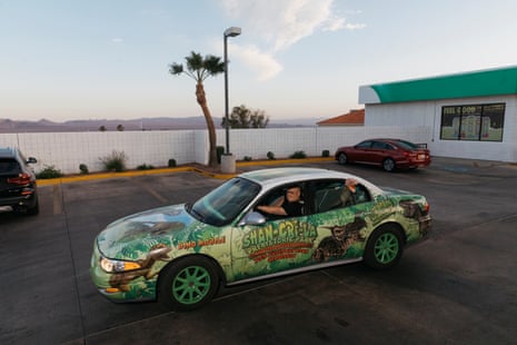 a man drives away in a dinasaur-themed car at a gas station