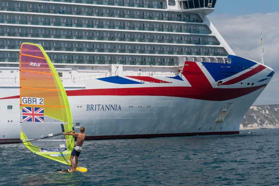 Tom Squires windsurfing past the MV Britannia P&O cruise ship at Weymouth Bay in Portland, Dorset during July 2020. At the time, seven large cruise ships were docked at Weymouth Bay due to the Covid-19 pandemic.