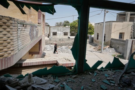 A person walks past rubble from a strike, seen through a shattered window frame