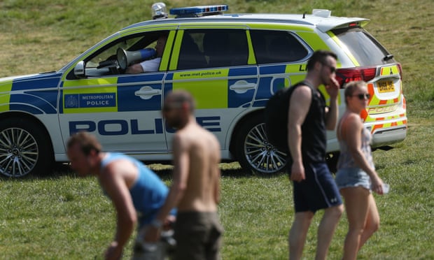 Police officers in a patrol car move sunbathers on in Greenwich park