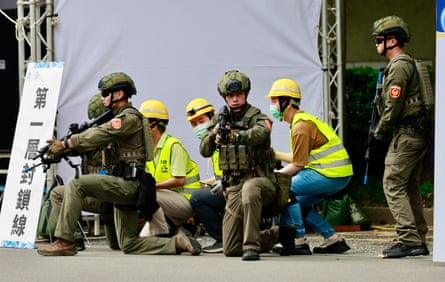 Four soldiers with guns, alongside three people in hi-vis vests