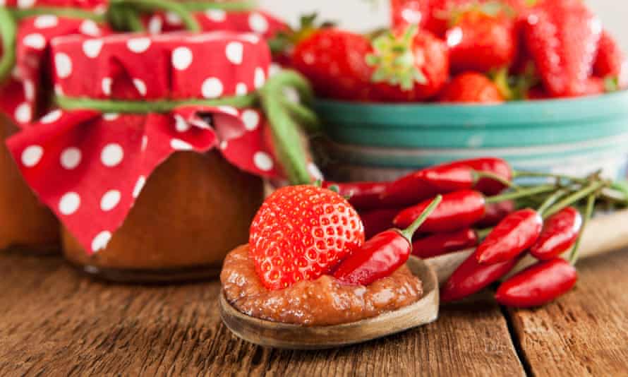 Strawberry and chilli jam on a wooden spoon, topped with a strawberry and a red chilli.