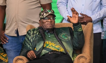 Jacob Zuma sitting in a chair, waving.