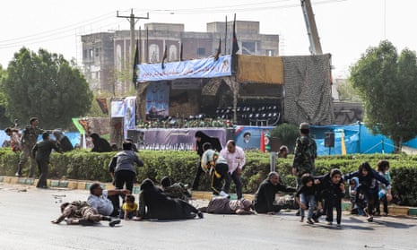 Iranian men, women, and children lying on ground and some seeking cover at the scene of the attack on a military parade.
