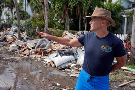Man in hat gestures toward street piled with debris.