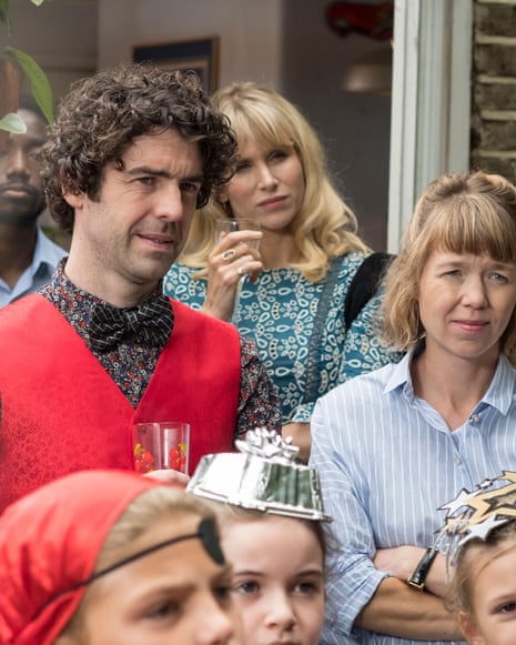 Paul Ready, Lucy Punch and Anna Maxwell Martin standing among other parents and children in a garden, with the children wearing costumes