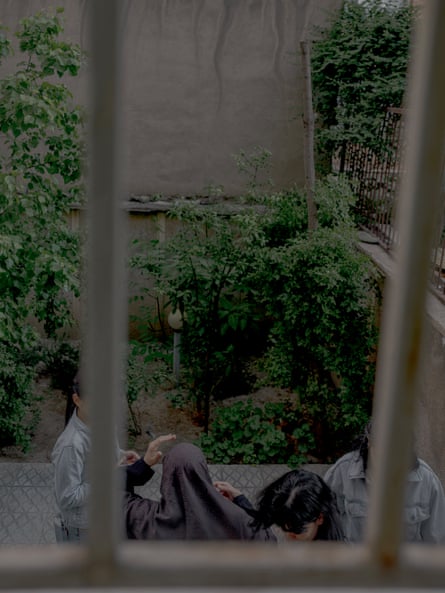 A group of women are seen through a window, standing outside by a garden. Their faces are obscured by the window frame.