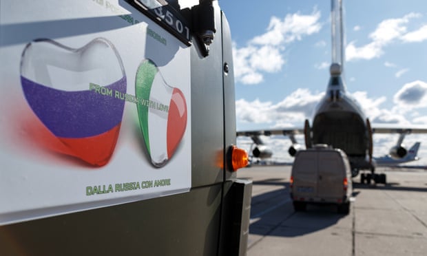 The side of a truck bearing Russian and Italian flags in the shape of love hearts next to a military plane being loaded with aid supplies