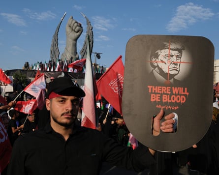 A man in Tehran holds up a picture of Donald Trump in the crosshairs of a sniper rifle with the text ‘there will be blood’ over it