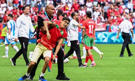 A Morocco supporter is taken off the pitch by a member of security during the pitch invasions that marred their contest with Argentina in Saint-Etienne