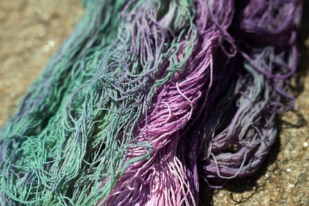 Skeins of green and purple yarn lying on sand
