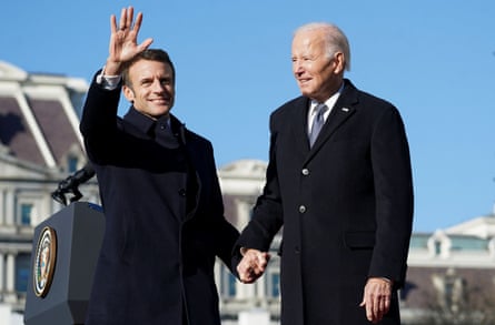 Emmanuel Macron waves and holds hands with Joe Biden on a stage outside the White House.