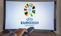 Man presses remote control for smartscreen TV showing Euros 2024 logo