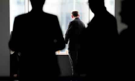 Silhouette of three men flank a man in a dark suit looking out of a window.