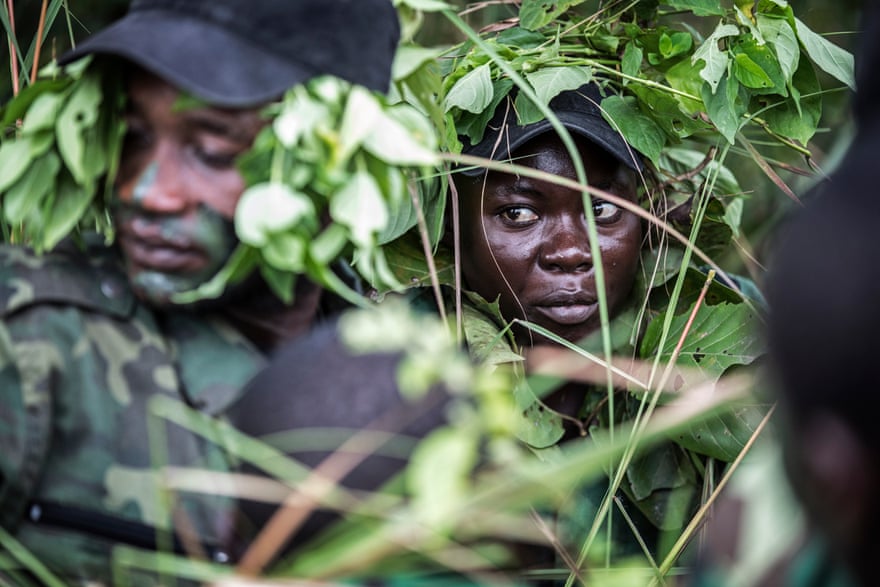 A female Gabon national park ranger sits with other rangers in the dense undergrowth of a rainforest.