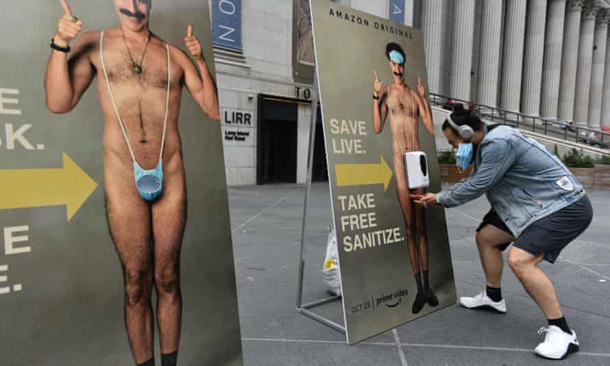 People take a free face mask and squirt of hand sanitiser from a promotional poster of Borat Subsequent Moviefilm, New York, October 2020.
