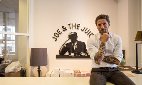 Kaspar Basse sitting in a Joe and the Juice office decorated in pale cream tones, with a large company logo on the wall behind him