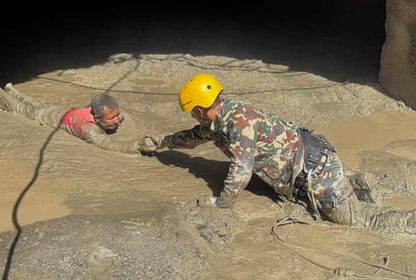 A rescuer pulls a survivor through the thick mud to safety.
