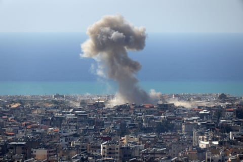 A column of smoke rises high into a blue sky above a residential neighbourhood with the sea in the background