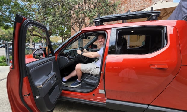Jake Whitehead sits in a red Rivian electric ute with the driver door open