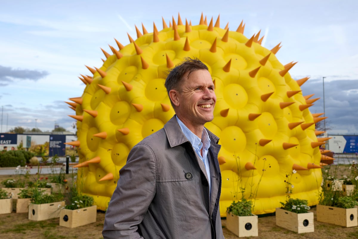 Luke Jerram in front of his Pollenarium art installation. It is a very large, yellow, inflatable sphere with orange spikes all over its surface.