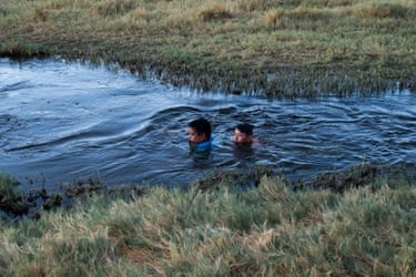 Two people in swim in a river surrounded by vegetation.