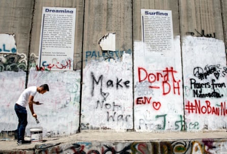 A young Palestinian checks his phone while painting the separation wall in Bethlehem to make space on the wall for tourists to spray their own messages near the new hotel set up by the British graffiti artist Banksy