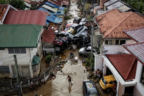 A man crosses a muddy street where cars are piled up and smashed together