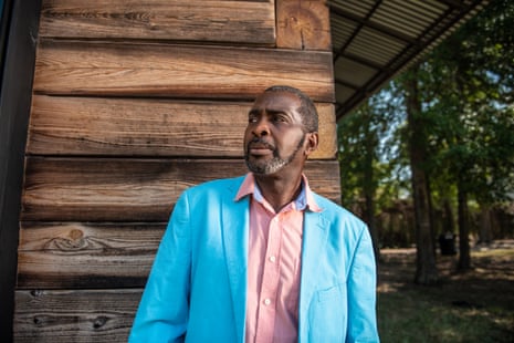 man in a blue blazer standing in front of a wooden building