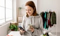 Female owner using cell phone and drinking coffee while standing in home office - Freelancer worker and small business concept