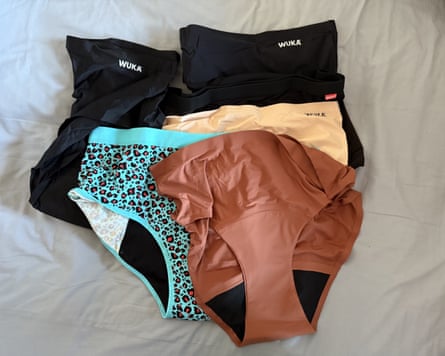 Six pairs of period pants lay on top of each other on a bed sheet