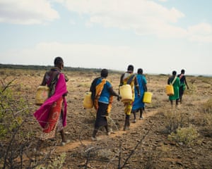A line of women in Ltungai walk to a water hole to fill their yellow jerry cans