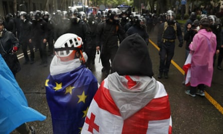 riot police and protesters one with EU flag and another with Georgian flag.