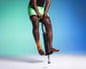 A man wearing green shorts and with a support on his ankle bouncing on a pogo stick against a graduated blue and green background