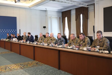 A dozen negotiators in military fatigues behind a long wooden desk