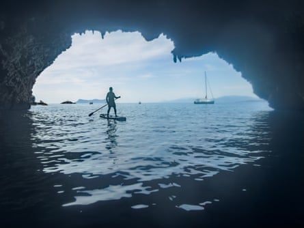 Vista di un uomo che pratica paddleboarding dall'ingresso buio di una grotta marina.