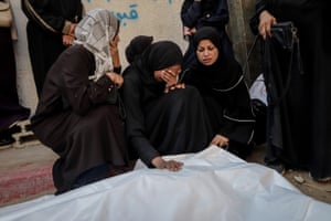 A woman holds one hand over her face and places the other on a body bag