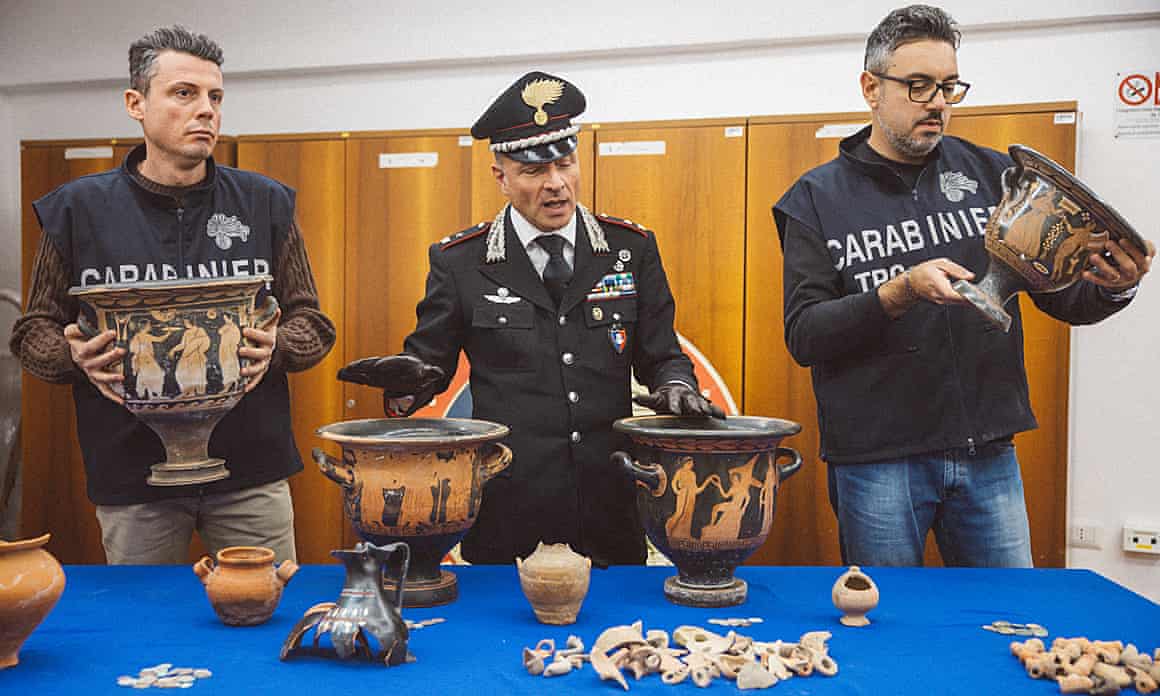 Three officers display Greek vases and other artifacts