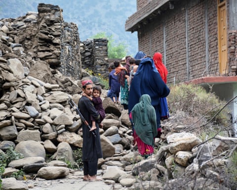 A man holds a child as a line of others pick their way through rubble