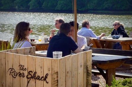 People dining at simple outdoor tables by a river