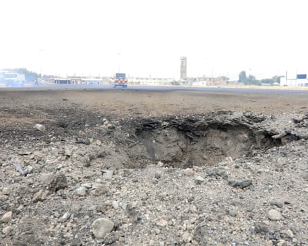 Closeup of a crater in the runway, with emergency vehicles in the distance