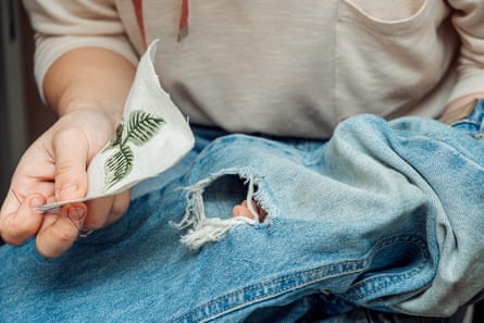 A woman mends jeans, sews a patch on a hole, hands close up