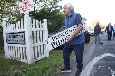 A man holding a ‘Principality of Piddington’ sign at the village boundary in Piddington, Oxfordshire.