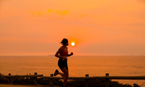 Woman running against setting orange sun