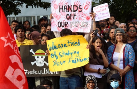 Someone in a crowd holds up a sign that says: ‘We are tired of studying your failures’