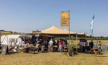A festival pub in a field on a sunny day, with a sign that reads ‘The Earthworm Arms’.