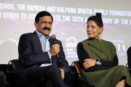 A man and a woman sit in front of a screen, the man holds a microphone