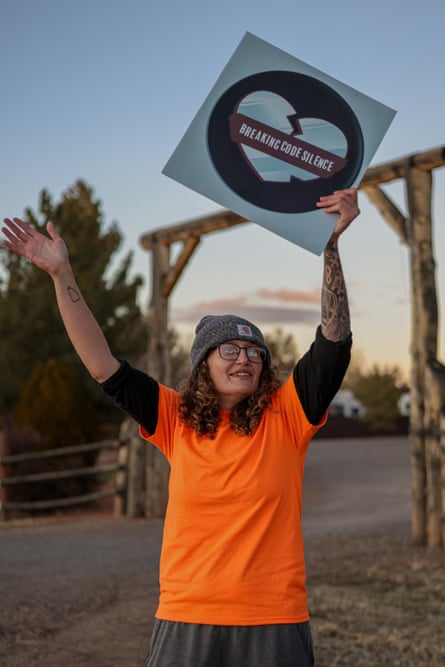 a woman holds a sign with a broken heart that reads ‘breaking code silence’