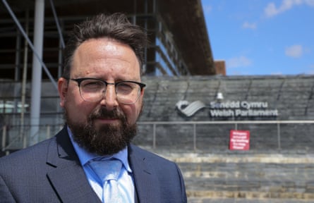 Man in glasses stands in front of Welsh parliament.